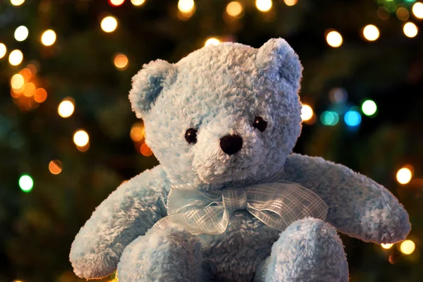 Ein blauer Teddybär sitzt vor einem Hintergrund aus schimmerndem Weihnachtsbaum. — Stockfoto
