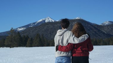 A couple gazes across a field of winter snow at the majestic peaks of the S clipart
