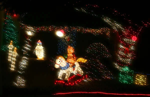 Un osito de peluche monta un caballo mecedora en una exhibición de luces navideña — Foto de Stock