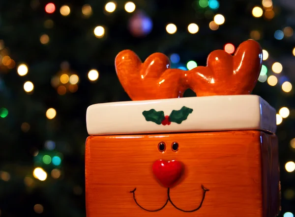 A Rudolph the Red Nosed Reindeer candy dish sits before a background of shi — Stock Photo, Image