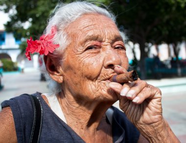 Old wrinkled woman with red flower smoking cigar clipart