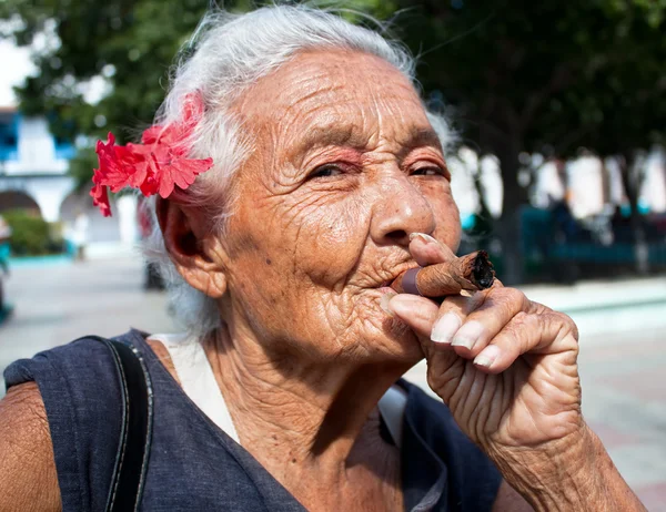 Vecchia donna rugosa con fiore rosso fumare sigaro — Foto Stock