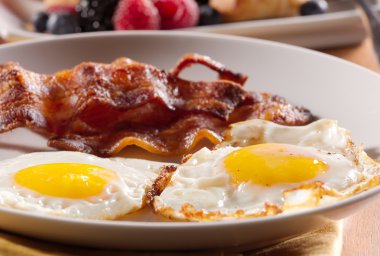 Sunny side up eggs with fried bacon. clipart