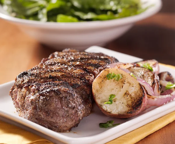 Ужин со стейком с картошкой и салатом на заднем плане — стоковое фото