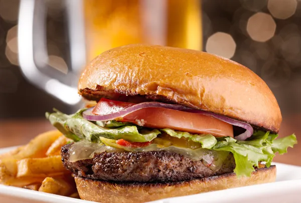 Gourmet cheeseburger with mug of beer in background — Stock Photo, Image