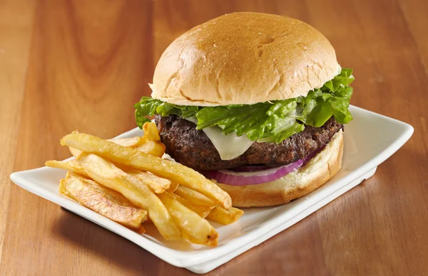 Гамбургер с сыром, салатом, луком с картошкой фри. Селективный акцент на бургере — стоковое фото