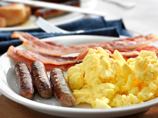 Breakfast meal with sausage and scrambled eggs with bacon.