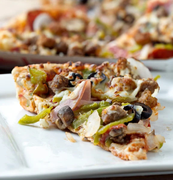 Rebanada de pizza con ingredientes supremos en un plato —  Fotos de Stock