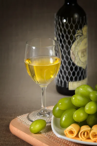 Un bicchiere di vino bianco, uva verde e una bottiglia di vino su una superficie di legno — Foto Stock