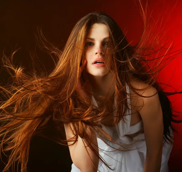 Hermosa mujer con el pelo largo y fluido sobre un fondo rojo —  Fotos de Stock