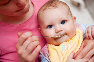 Mother feeding baby food to baby clipart