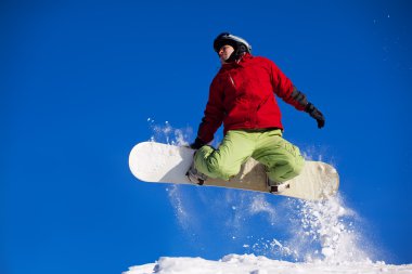 Snowboarder jumping through air with deep blue sky in background clipart