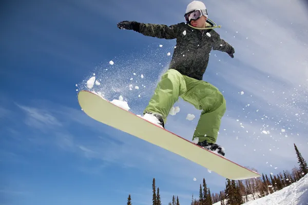 Snowboardåkare hoppa genom luften skogen i bakgrunden — Stockfoto