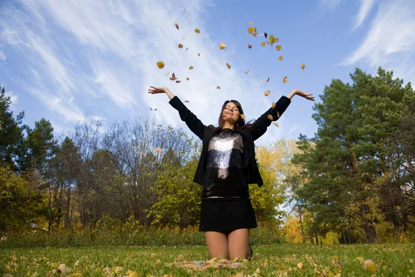 Jovem mulher jogar folhas outonais — Fotografia de Stock