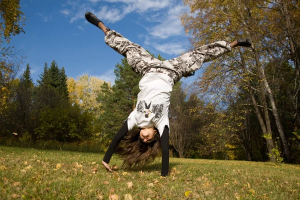 Uma jovem mulher faz um suporte na grama na frente do céu azul — Fotografia de Stock