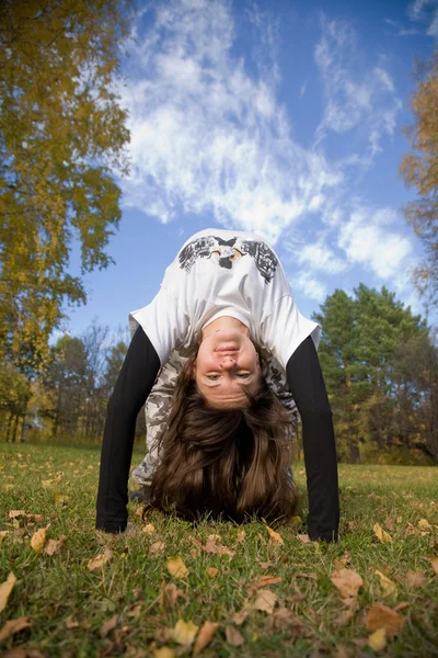 Een jonge vrouw maakt een handstand op gras voor blauwe hemel — Stockfoto