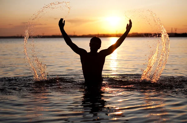 stock image Young man in water. Sunset background