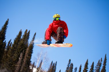 Snowboarder jumping through air with blue sky in background clipart