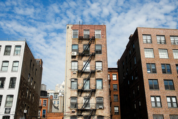 Edificios con escaleras exteriores de Manhattan, Nueva York con sol y nubes