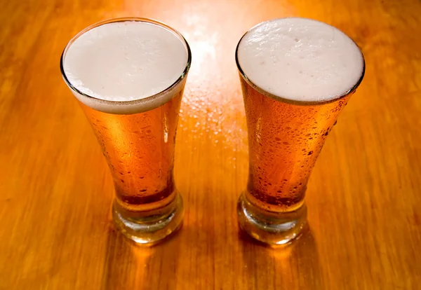 Dois copos de cerveja no fundo de madeira molhada — Fotografia de Stock