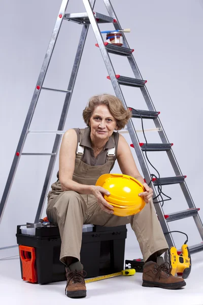 Senior mulher sentada em uma caixa de ferramentas — Fotografia de Stock