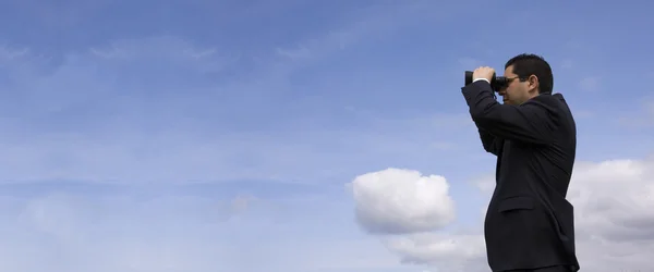 Бізнесмен дивиться через бінокль з блакитним небом як фон — стокове фото