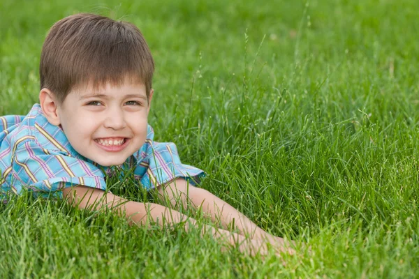 Улыбающийся мальчик на зеленой лужайке — стоковое фото