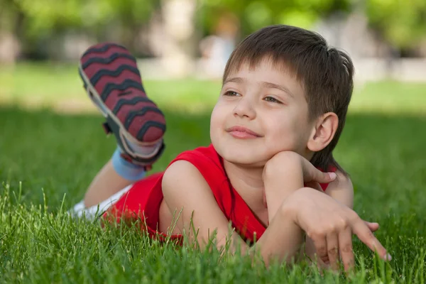 Задумчивый красивый мальчик на зеленой траве — стоковое фото