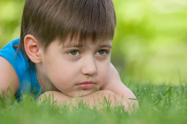 Задумчивый мальчик на зеленой траве — стоковое фото