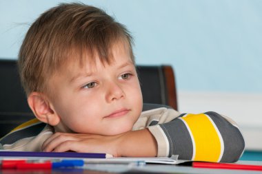 A thoughtful little boy at the desk clipart