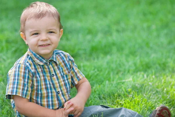 Closeup portrait of a smiling boy against the green grass — Stock Photo, Image