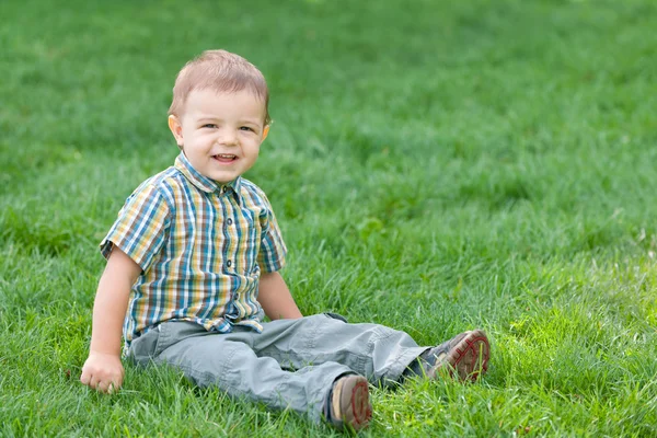 Улыбающийся мальчик на зеленой летней траве — стоковое фото