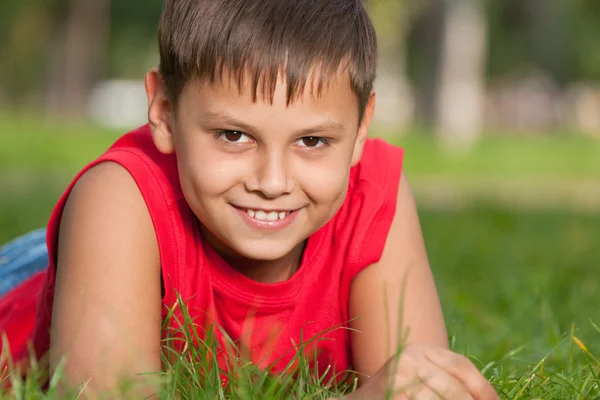 Usměvavý chlapec v červené barvě na trávě — Stock fotografie
