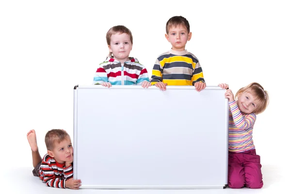 Quatro crianças segurando uma prancha branca — Fotografia de Stock