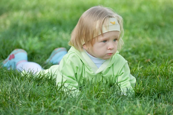 Pensativo niño se arrastra en la hierba verde — Foto de Stock