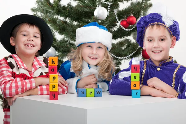 Three children dressed in carnival suits are greeting with sigh "happy — Stock Photo, Image