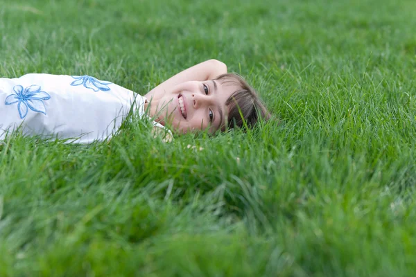 Retrato de uma menina sorrindo olhando para fora da grama verde — Fotografia de Stock