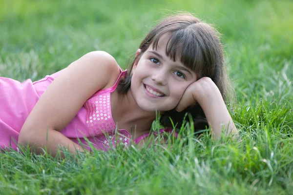 Retrato de una niña de color rosa acostada sobre la hierba verde y sosteniendo —  Fotos de Stock
