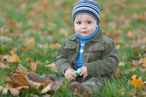 Menino sentado na grama de outono — Fotografia de Stock
