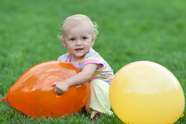 Hübsches kleines Mädchen spielt mit gelben und roten Luftballons auf Gras — Stockfoto