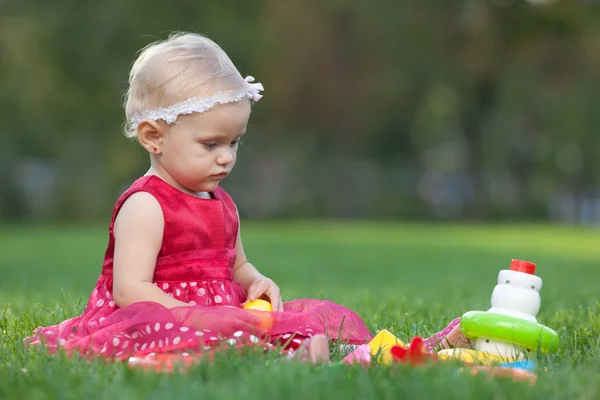 Pretty blond little girl is playing with toy pyramid on grass — Stock Photo, Image