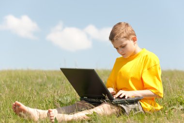 Çocuk çayır üzerinde oturan laptop üzerinde çalışıyor