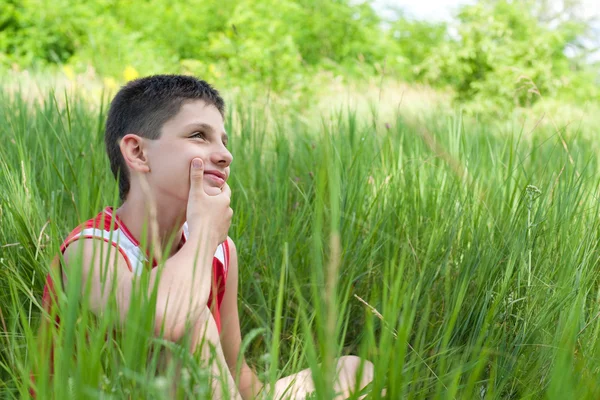 Задумчивый мальчик в зеленой траве — стоковое фото