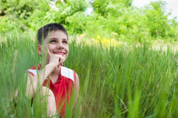 Улыбающийся мальчик в зеленой траве — стоковое фото