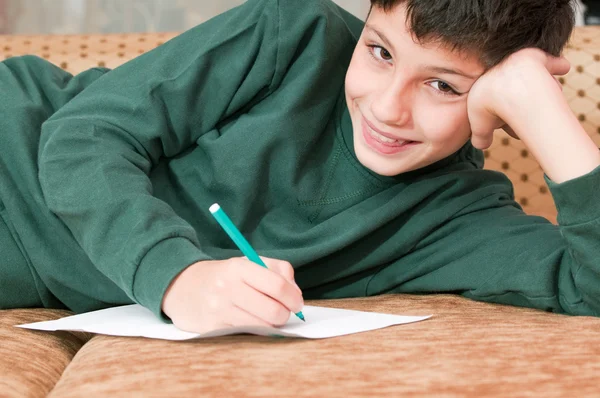 Un garçon souriant écrit une lettre — Photo