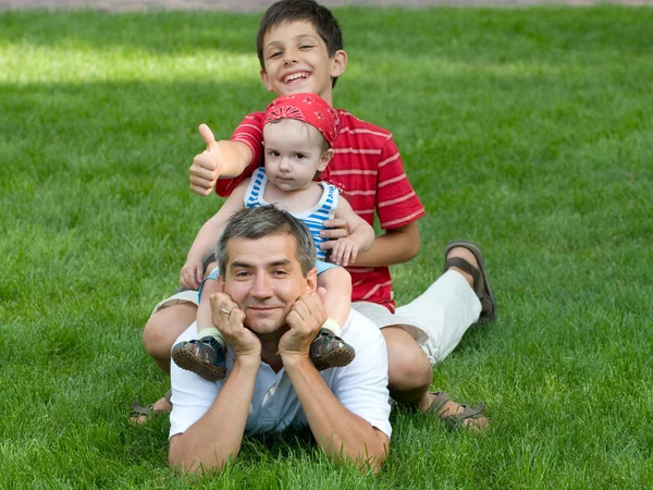 Dos hijos están sentados en la espalda de su padre. — Foto de Stock