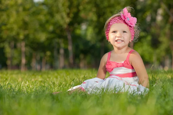 Cheerful little girl on the grass in the park — Stock Photo, Image