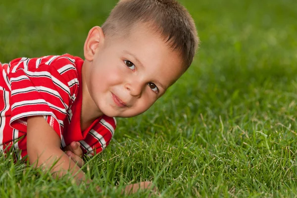 Kleine jongen in het rood op het groene gras — Stockfoto