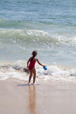 Küçük kız sahilde kovayla oynuyor.