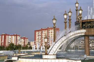 Fountain with lampposts and some living building. clipart